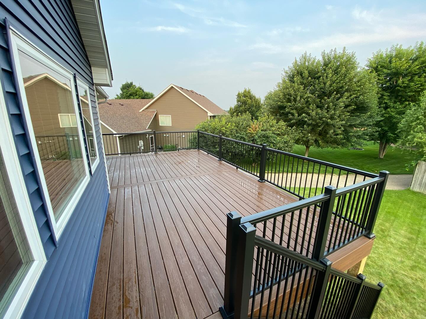 Mahogany-toned composite deck with black aluminum railing after a rain