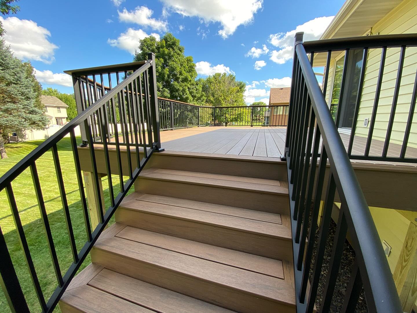 View up the composite stairs to a spacious two-tone backyard deck
