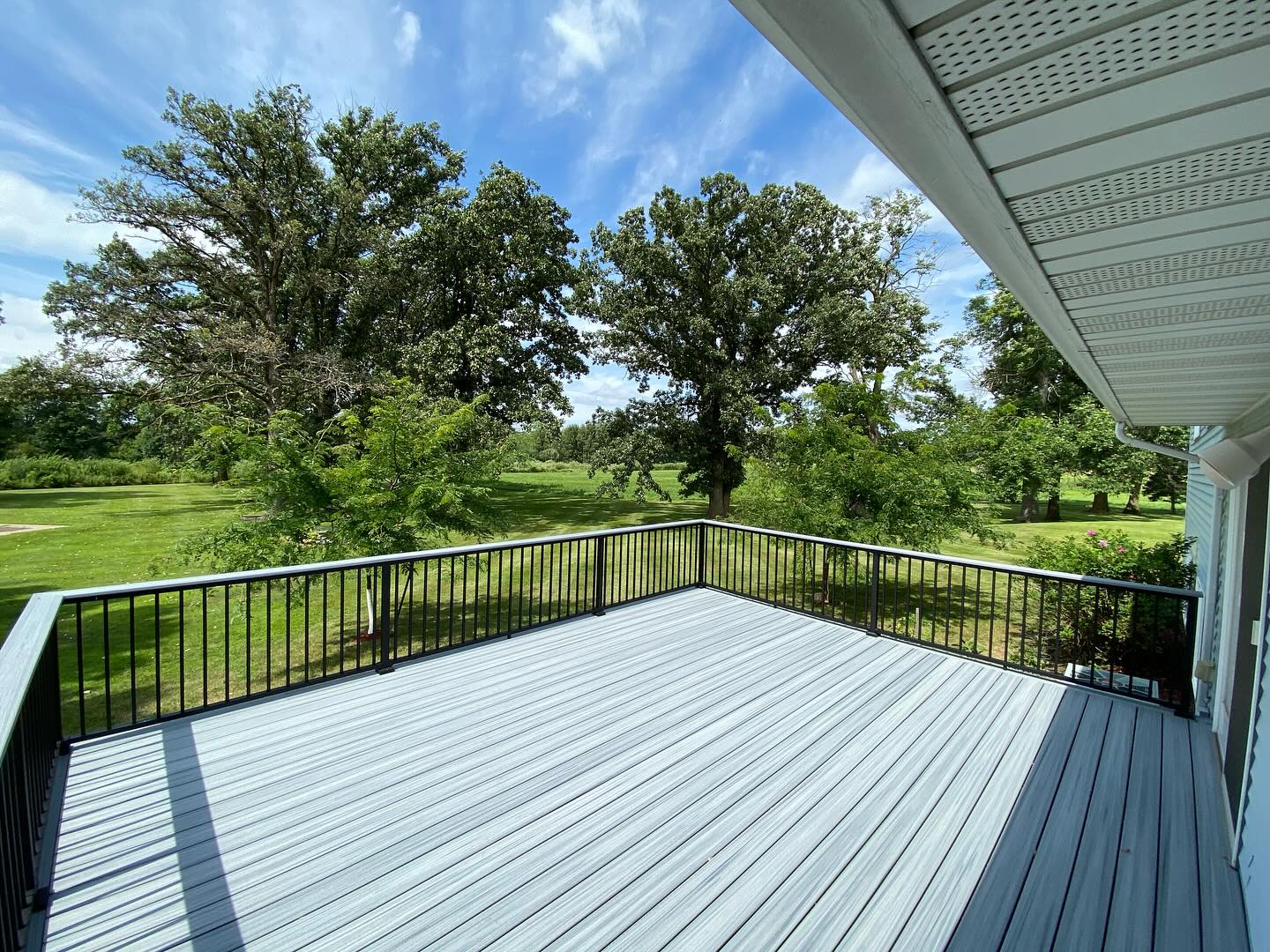 Composite deck with black metal railing and mature oak tree views