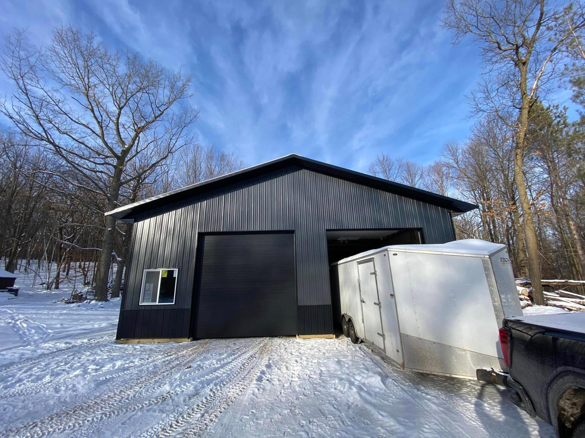 Black steel pole barn garage with oversized overhead door in a wooded lot