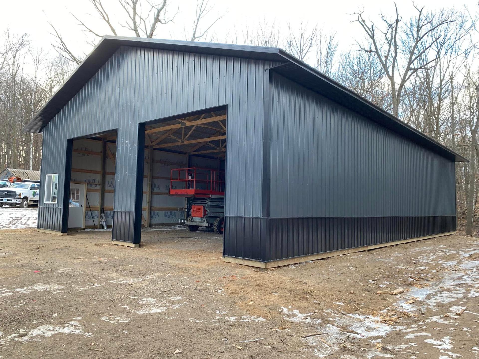 Large gray pole-frame warehouse with two open overhead doors during construction