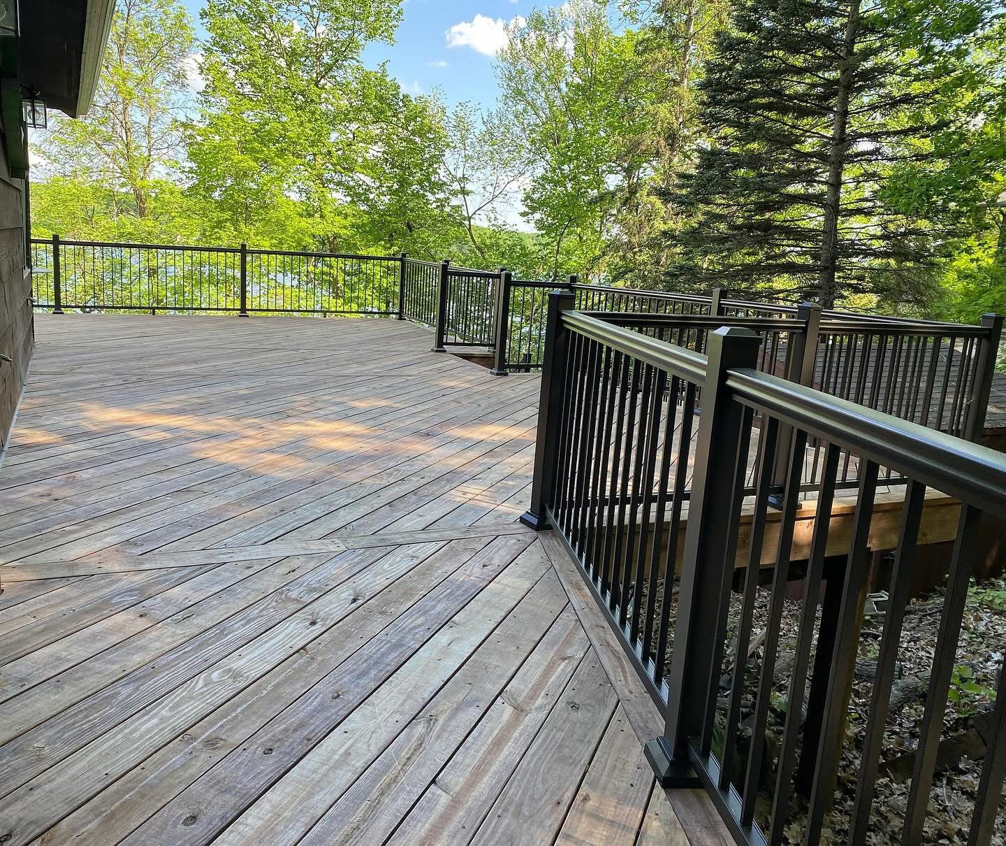 Wood deck with black aluminum railing overlooking wooded lake views